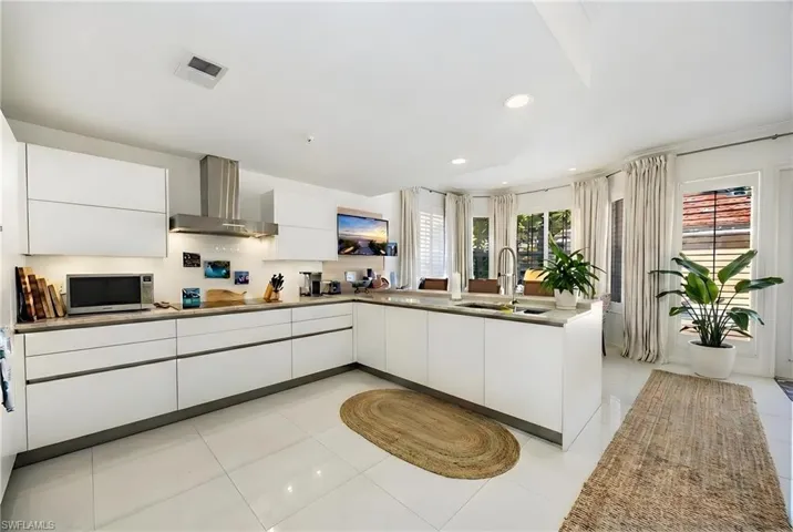 Kitchen with a peninsula, modern cabinets, white cabinets, stainless steel microwave, and light tile patterned flooring