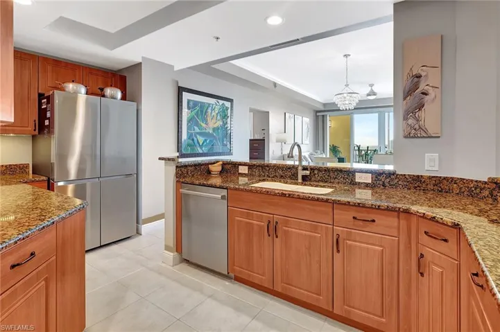 Kitchen featuring dark stone countertops, sink, a tray ceiling, stainless steel appliances, and hanging light fixtures