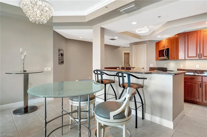 Kitchen with a kitchen bar, hanging light fixtures, light tile patterned floors, dark stone countertops, and ornamental molding