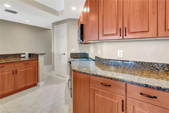 Kitchen featuring stainless steel range with electric stovetop, light tile patterned floors, and dark stone counters