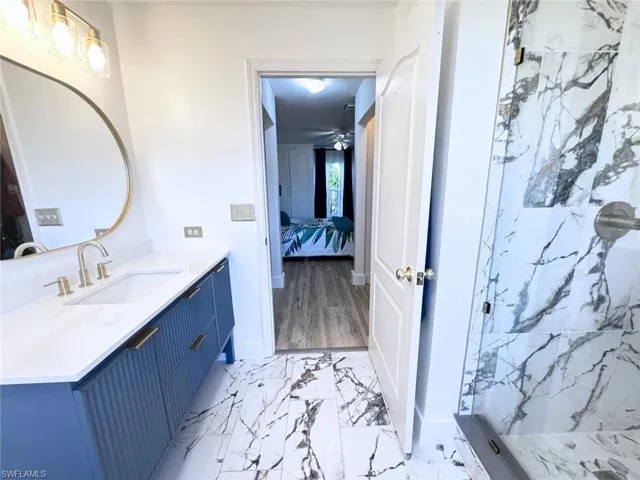Ensuite bathroom featuring marble-look tile floor, a marble finish shower, baseboards, and vanity, connect to bedroom with two closets in the corridor