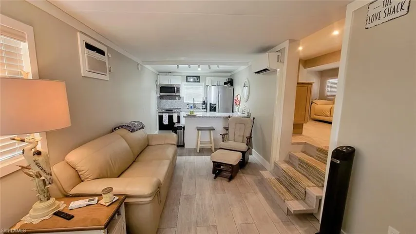 Living area featuring light wood-type flooring, ornamental molding, and an AC wall unit