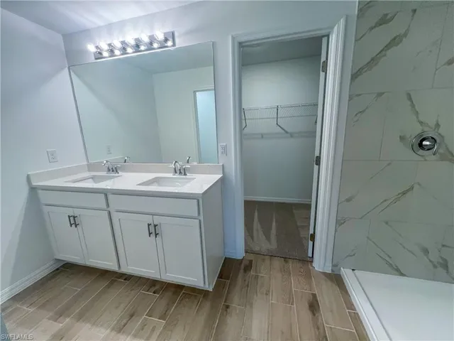 Bathroom featuring wood finish floors, double vanity, a spacious closet, and a marble finish shower