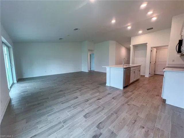 Kitchen featuring wood tiled floors, a kitchen island with sink, open floor plan, white cabinets, and recessed lighting