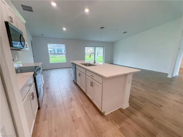Kitchen with white cabinets, appliances with stainless steel finishes, open floor plan, light wood finished floors, and recessed lighting