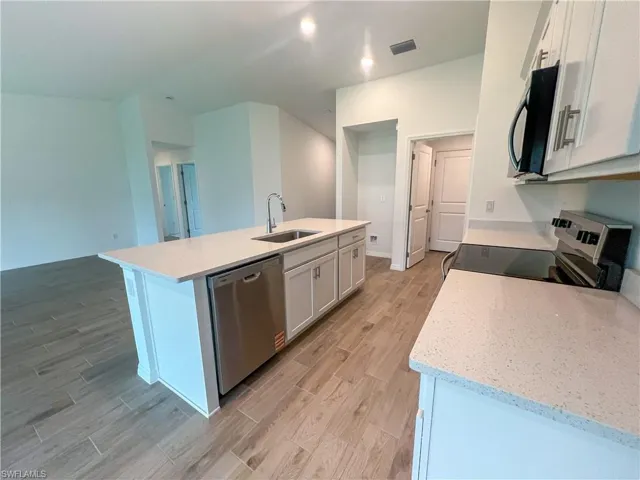 Kitchen with stainless steel appliances, light stone countertops, wood tiled floors, a kitchen island with sink, and white cabinets