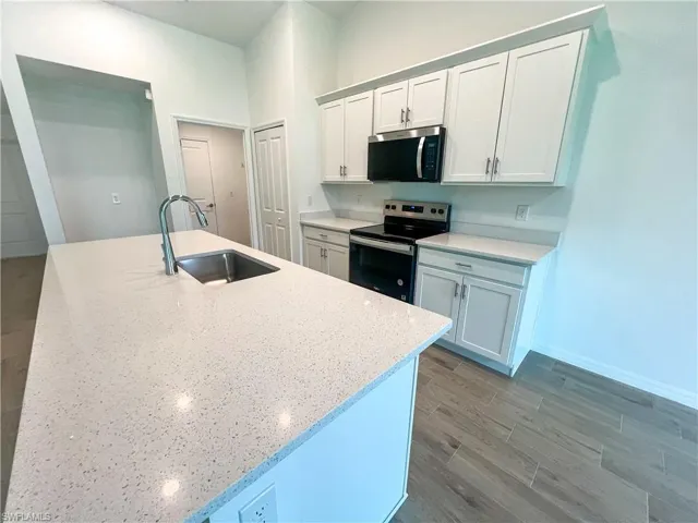 Kitchen with stainless steel appliances, light wood-style flooring, light stone countertops, and a center island with sink