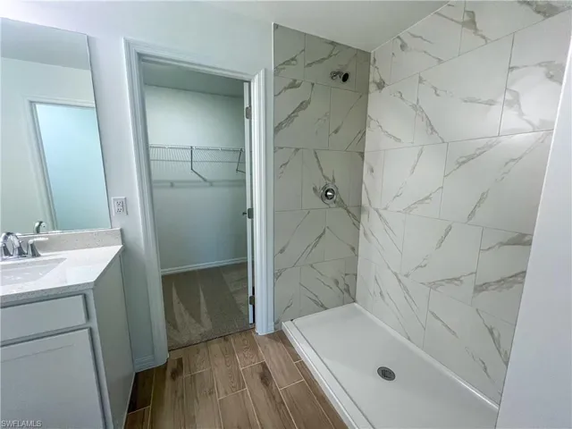 Bathroom with a walk in closet, vanity, a stall shower, and wood tiled floors