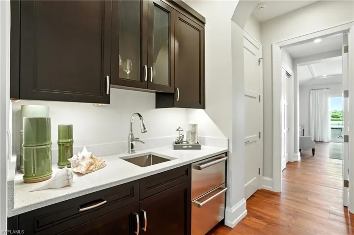 Kitchen with dark brown cabinets, light wood-style flooring, light stone countertops, and stainless steel dishwasher