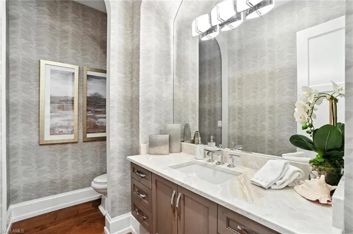 Half bath featuring wallpapered walls, vanity, and dark wood-type flooring