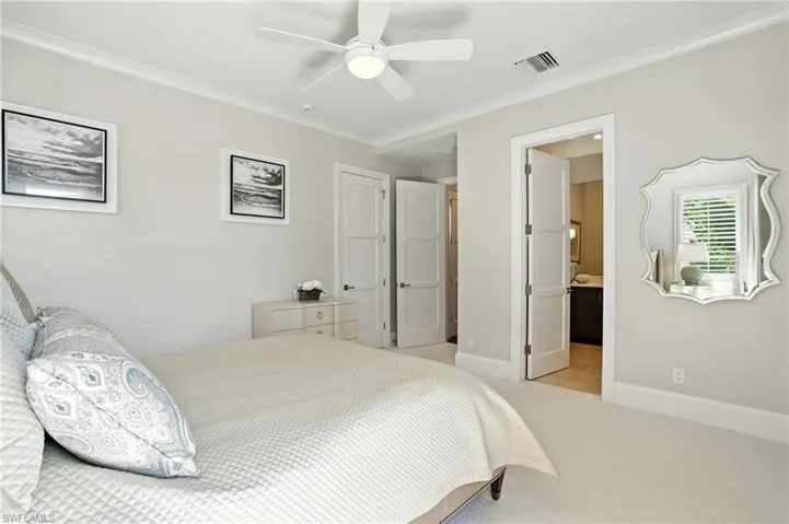 Bedroom with ornamental molding, light carpet, a ceiling fan, and ensuite bath