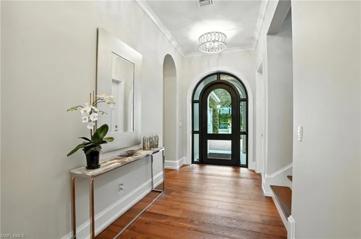 Entrance foyer featuring crown molding, hardwood / wood-style flooring, arched walkways, and a chandelier