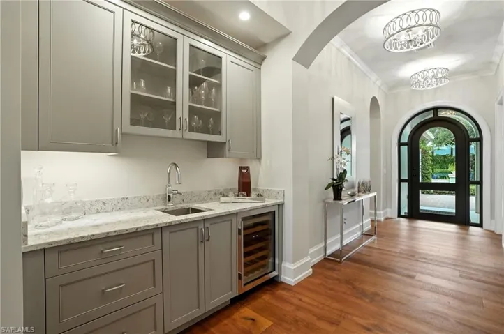 Bar with gray cabinets, arched walkways, crown molding, glass insert cabinets, and light stone countertops