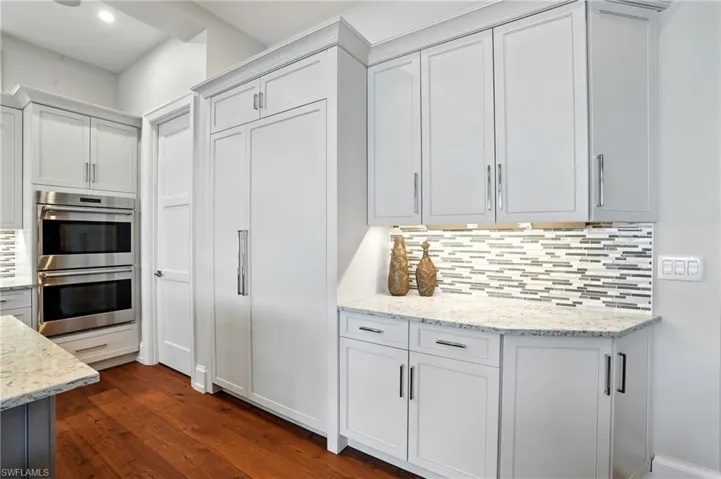 Kitchen featuring backsplash, light stone countertops, double oven, white cabinetry, and dark wood finished floors