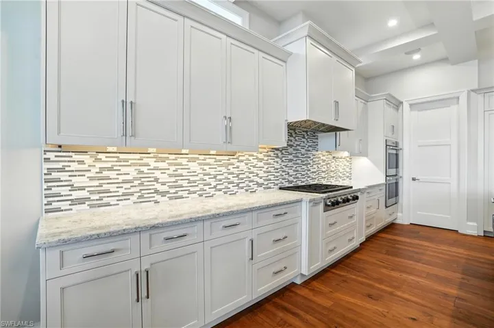 Kitchen with dark wood-style flooring, light stone countertops, tasteful backsplash, white cabinetry, and recessed lighting