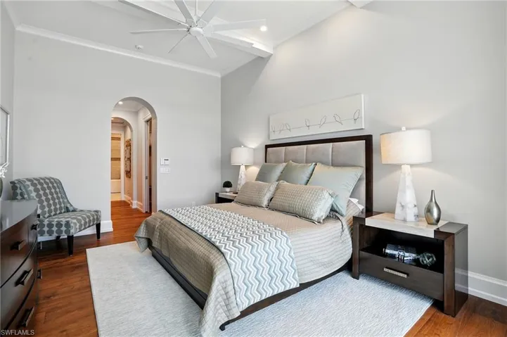 Bedroom with arched walkways, dark wood-style flooring, ceiling fan, and crown molding