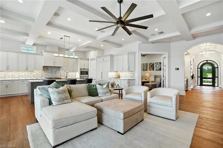 Living area featuring coffered ceiling, beamed ceiling, arched walkways, wood finished floors, and a ceiling fan