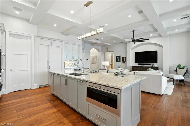 Kitchen featuring coffered ceiling, arched walkways, beamed ceiling, hanging light fixtures, and light stone countertops