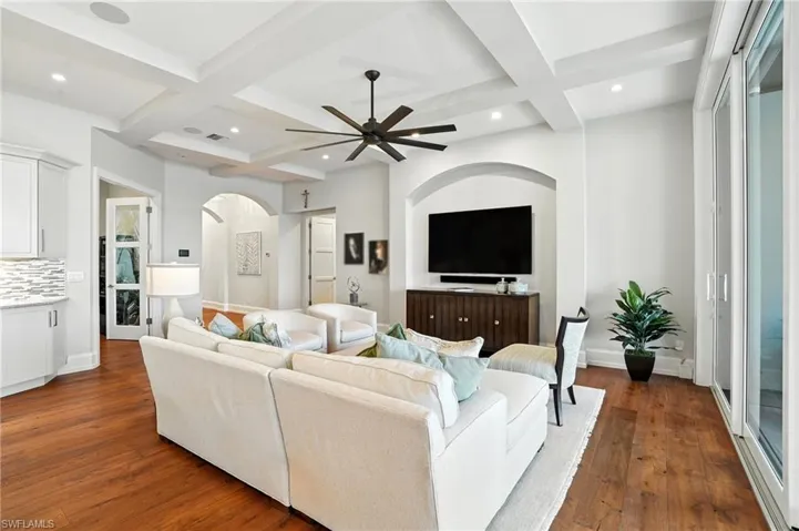 Living room with coffered ceiling, beamed ceiling, dark wood finished floors, arched walkways, and ceiling fan