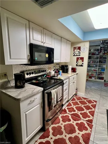 Kitchen with electric stove, white cabinets, light countertops, black microwave, and light tile patterned floors
