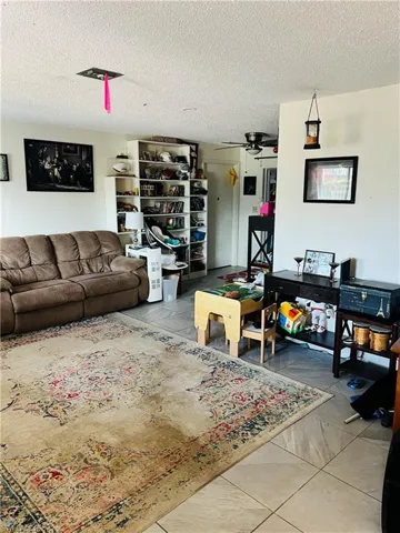 Living area with ceiling fan, a textured ceiling, and light tile patterned floors