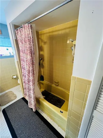 Full bathroom with shower / tub combo with curtain, tile patterned flooring, and tile walls