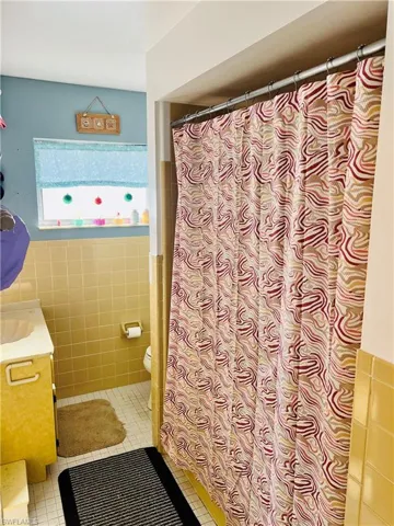 Full bathroom featuring vanity, tile walls, curtained shower, and light tile patterned floors