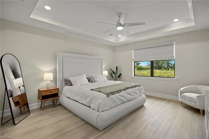 Bedroom with ceiling fan, ornamental molding, a tray ceiling, and light hardwood / wood-style floors