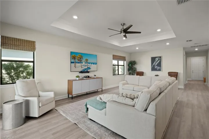 Living room featuring ceiling fan, a raised ceiling, crown molding, and light hardwood / wood-style flooring
