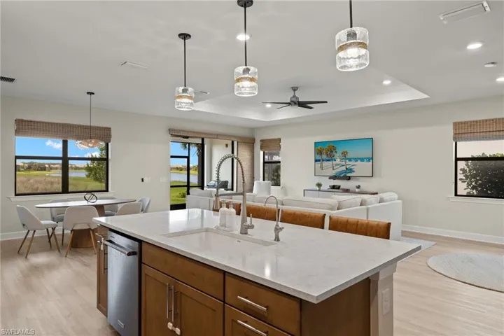Kitchen with hanging light fixtures, light hardwood / wood-style floors, ceiling fan with notable chandelier, a kitchen island with sink, and sink