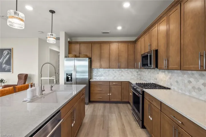 Kitchen featuring hanging light fixtures, backsplash, stainless steel appliances, light wood-type flooring, and sink