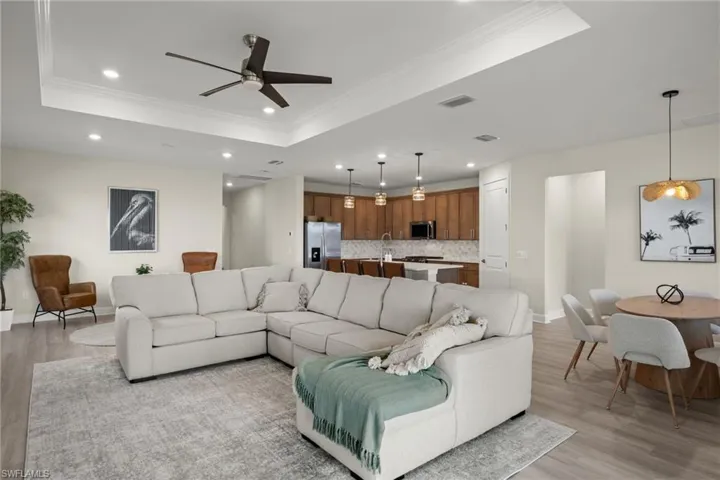 Living room with ornamental molding, light wood-type flooring, a tray ceiling, and ceiling fan