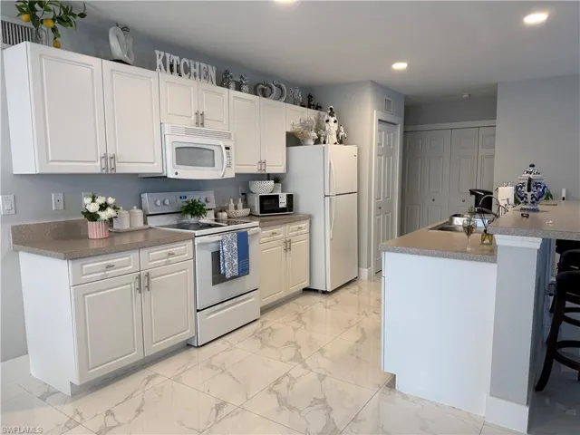 Kitchen with white appliances, a breakfast bar, white cabinetry, a center island with sink, and light marble finish floors