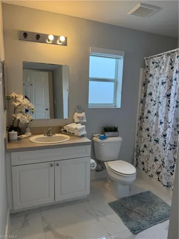 Full bath featuring vanity, a shower with curtain, light marble finish flooring, and a textured wall