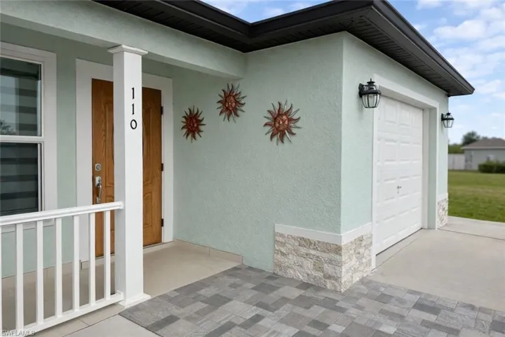 Doorway to property featuring a porch, an attached garage, stucco siding, stone siding, and concrete driveway