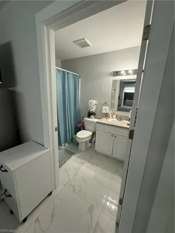 Bathroom featuring vanity, light marble finish floors, and a shower with curtain