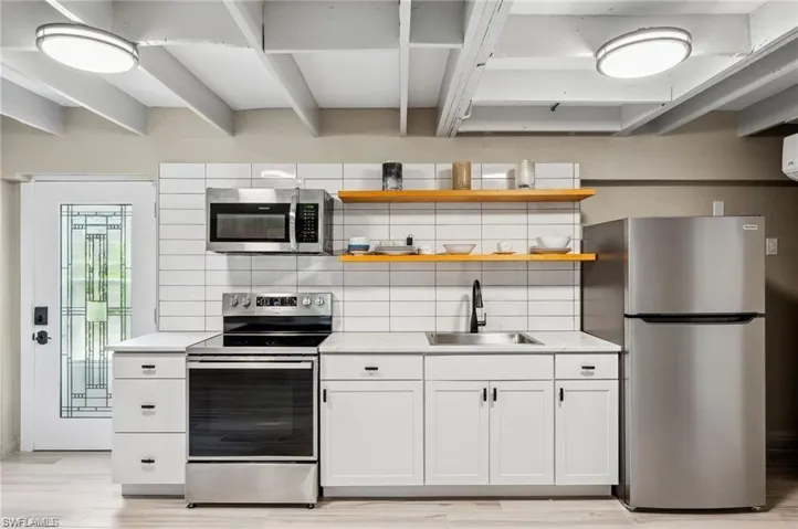 Kitchen featuring appliances with stainless steel finishes, backsplash, sink, white cabinets, and light hardwood / wood-style floors