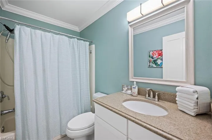 Full bathroom with shower / bath combo with shower curtain, vanity, toilet, and crown molding
