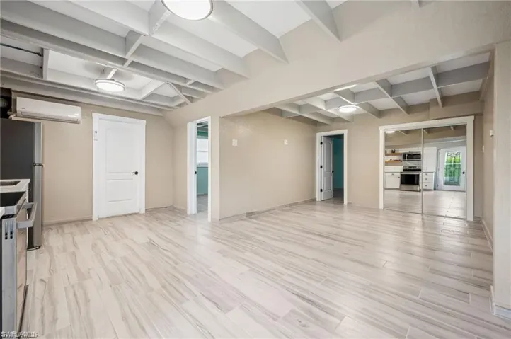 Unfurnished living room featuring a wall unit AC, light hardwood / wood-style flooring, and beam ceiling
