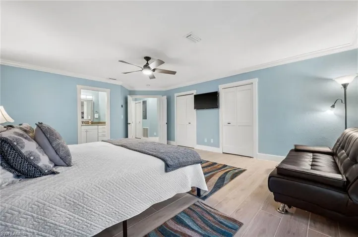 Bedroom with two closets, ensuite bathroom, ceiling fan, ornamental molding, and light hardwood / wood-style floors
