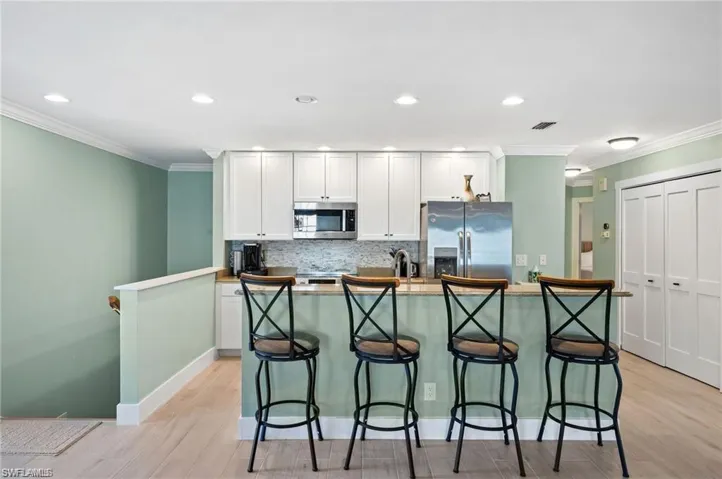 Kitchen with white cabinetry, an island with sink, light hardwood / wood-style floors, and appliances with stainless steel finishes