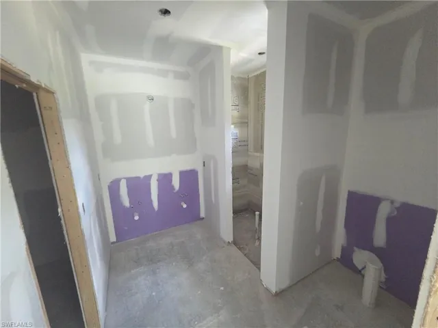 Interior space with unfinished drywall, purple water-resistant drywall panels, and a concrete floor
