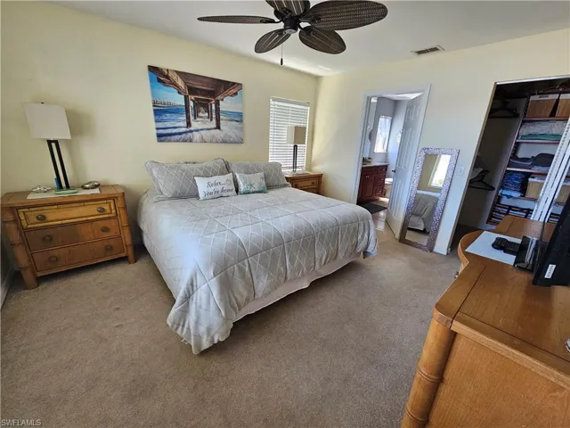 Bedroom with carpet flooring, connected bathroom, ceiling fan, and multiple windows