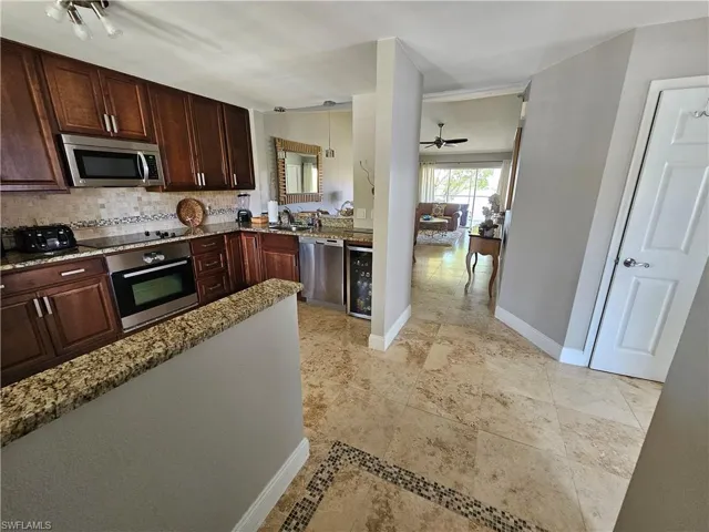 Kitchen with light stone counters, wine cooler, appliances with stainless steel finishes, and light tile floors