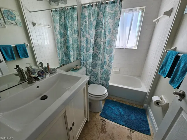 Full bathroom with tile flooring, shower / bath combo, large vanity, and toilet