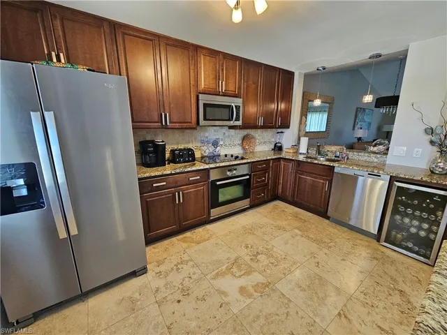 Kitchen with hanging light fixtures, appliances with stainless steel finishes, light stone counters, sink, and tasteful backsplash