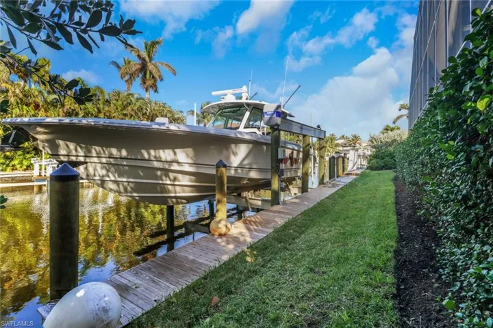 Dock area with boat lift, a yard, and a water view