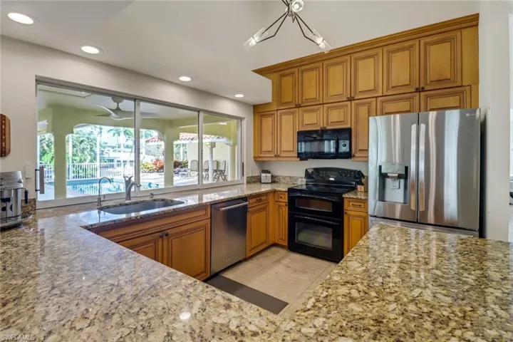 Kitchen with brown cabinets, light stone countertops, black appliances, recessed lighting, and light tile patterned floors