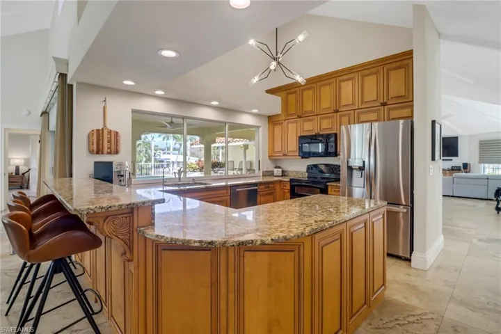 Kitchen with brown cabinetry, light stone counters, black appliances, a kitchen breakfast bar, and a peninsula