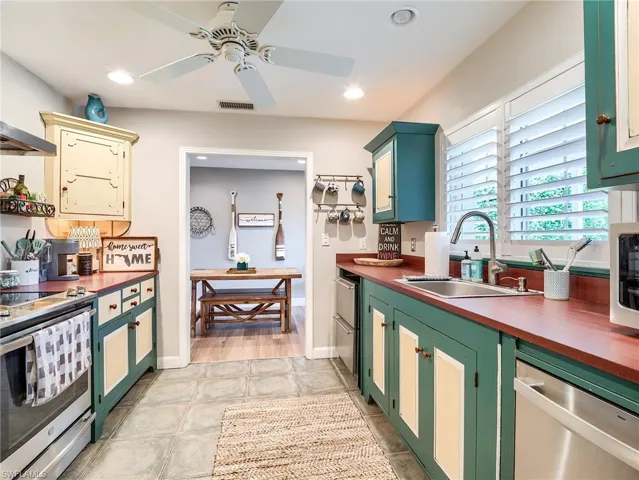 Kitchen featuring stainless steel dishwasher, butcher block countertops, range, light tile floors, and sink
